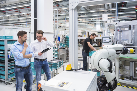 Man operating assembly robot in factory and two men talking stock photo