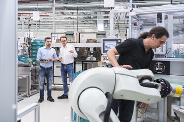 Man operating assembly robot in factory with two men in background supervising - DIGF02241