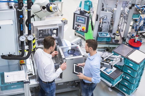 Zwei Männer mit Tablet im Gespräch in einer Fabrikhalle, lizenzfreies Stockfoto