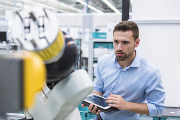 Man with tablet examining assembly robot in factory shop floor - DIGF02251
