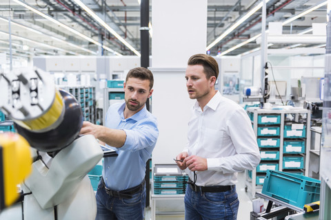 Zwei Männer mit Tablet, die einen Montageroboter in einer Fabrikhalle untersuchen, lizenzfreies Stockfoto