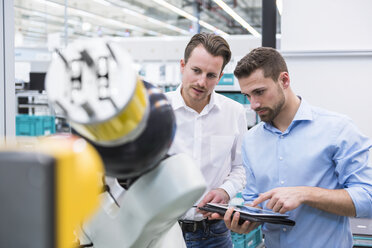 Zwei Männer mit Tablet, die einen Montageroboter in einer Fabrikhalle untersuchen - DIGF02253