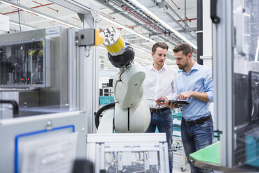 Zwei Männer mit Tablet, die einen Montageroboter in einer Fabrikhalle untersuchen - DIGF02254