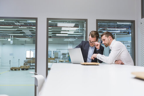 Zwei Geschäftsleute sitzen in einem modernen Büro und diskutieren vor einem Laptop - DIGF02272