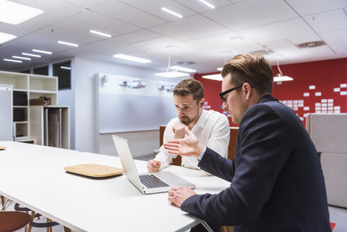 Zwei Geschäftsleute sitzen in einem modernen Büro und diskutieren vor einem Laptop - DIGF02276