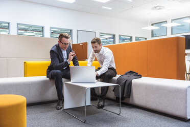 Businessmen sitting in conversation pit, discussing in front of laptop - DIGF02277