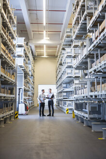 Two men talking in factory warehouse - DIGF02305