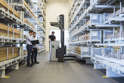 Two men with documents and worker with forklift in factory warehouse - DIGF02313