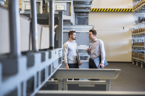 Zwei Männer unterhalten sich in einem Fabriklager, lizenzfreies Stockfoto