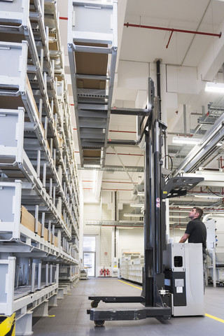 Worker operating forklift in factory warehouse stock photo