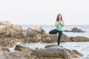 Frau übt Yoga auf einem Felsen am Meer - MOMF00165