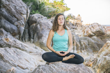 Frau meditiert auf einem Felsen am Meer - MOMF00166