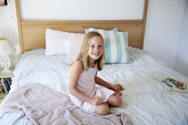 Porträt eines lächelnden kleinen Mädchens, das zu Hause auf dem Bett sitzt - SRYF00257