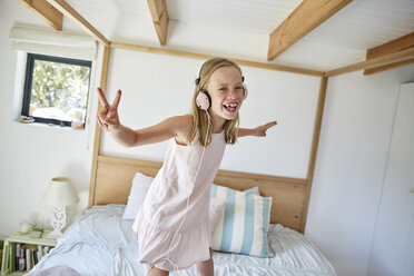 Porträt eines lächelnden kleinen Mädchens, das zu Hause auf dem Bett tanzt, während es mit Kopfhörern Musik hört - SRYF00259