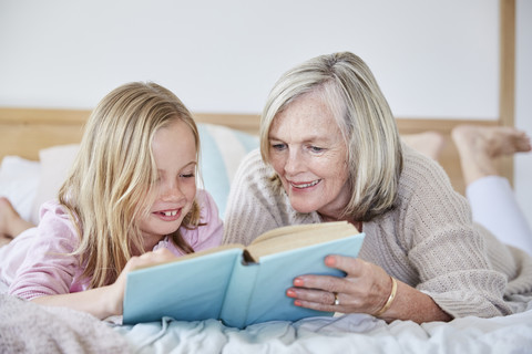 Little girl lying on the bed with her grandmother reading a book stock photo