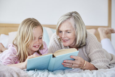 Little girl lying on the bed with her grandmother reading a book - SRYF00271
