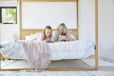Little girl lying on the bed with her grandmother reading a book - SRYF00273