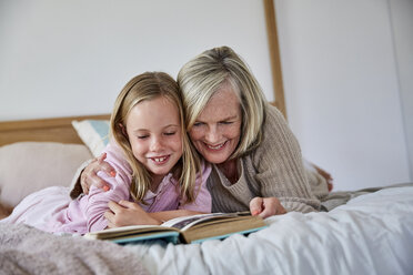 Little girl lying on the bed with her grandmother reading a book - SRYF00275