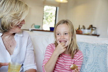 Porträt eines lächelnden kleinen Mädchens, das ein Sandwich isst, während die Großmutter sie beobachtet - SRYF00300