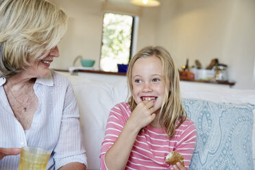 Portrait of smiling little girl eating sandwich while grandmother watching her - SRYF00300