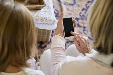 Rückansicht einer Großmutter, die neben ihrer Enkelin sitzt und ein Smartphone benutzt - SRYF00304