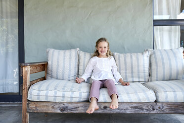 Porträt eines lächelnden blonden kleinen Mädchens, das auf einer Couch auf der Terrasse sitzt - SRYF00323