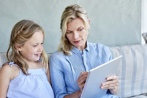 Mutter und kleine Tochter sitzen zusammen auf der Couch und schauen auf ein Tablet, lizenzfreies Stockfoto