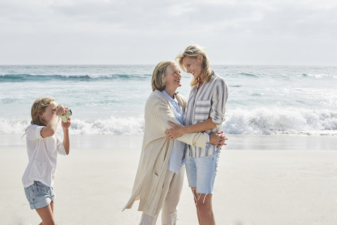 Little girl taking pictures on the beach of her mother and grandmother stock photo