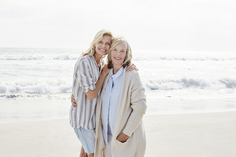 Ältere Frau und ihre erwachsene Tochter stehen am Strand und umarmen sich, lizenzfreies Stockfoto