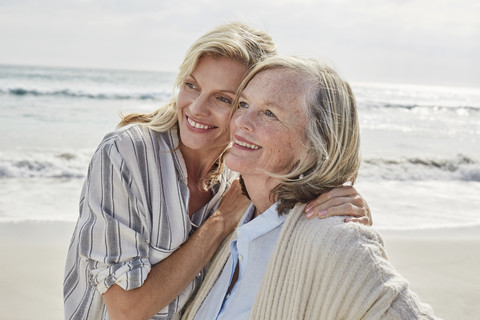 Senior woman and her adult daughter standing on the beach, embracing stock photo