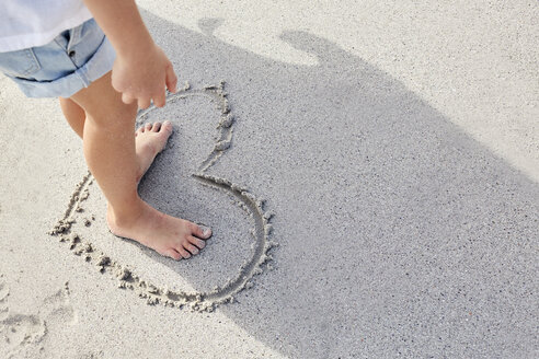 Little girl standing barefoot in a heart on sand - SRYF00351