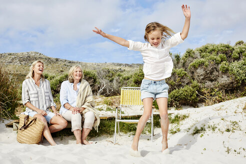 Mother, daughter and grandmother spending a day at the beach, girl jumping for joy - SRYF00365