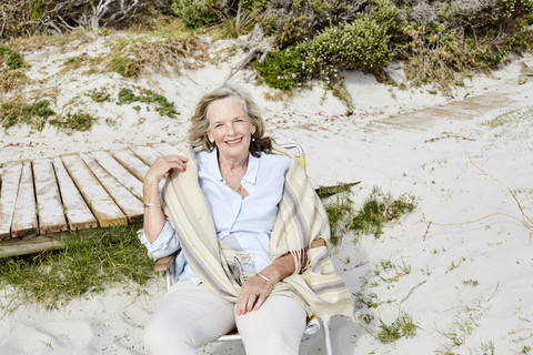 Ältere Frau sitzt am Strand und schaut in die Kamera, lizenzfreies Stockfoto