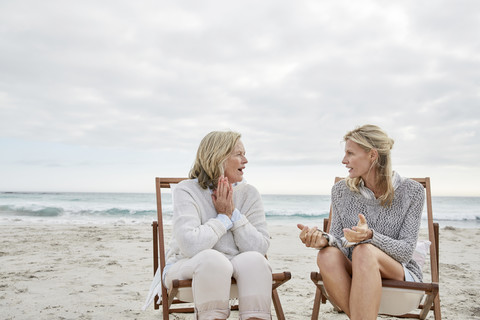 Mutter und Tochter unterhalten sich am Strand in Liegestühlen sitzend, lizenzfreies Stockfoto