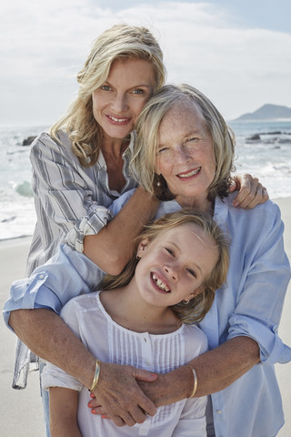 Mutter, Tochter und Großmutter umarmen sich am Strand, lizenzfreies Stockfoto