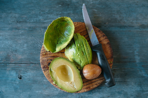 Sliced avocado, kernel and knife on wooden board stock photo