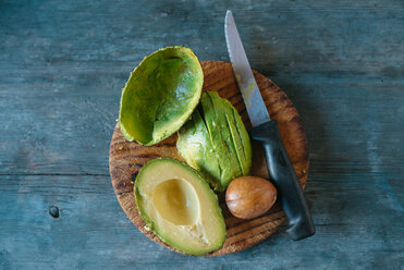 Sliced avocado, kernel and knife on wooden board - KIJF01415