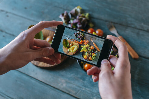 Nahaufnahme der Hände eines Mannes, der mit seinem Smartphone einen Avocadosalat fotografiert - KIJF01417