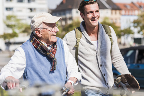 Happy senior man with adult grandson in the city on the move - UUF10415