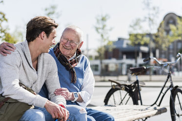 Glücklicher älterer Mann mit erwachsenem Enkel auf einer Bank sitzend - UUF10422