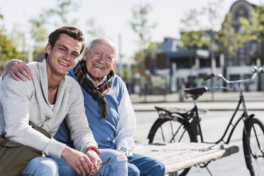 Portrait of happy senior man with adult grandson sitting on a bench - UUF10423