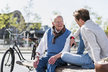 Älterer Mann und erwachsener Enkel unterhalten sich auf einer Bank - UUF10424