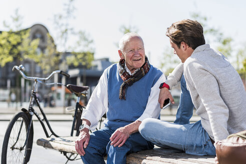 Senior man and adult grandson talking on a bench - UUF10424