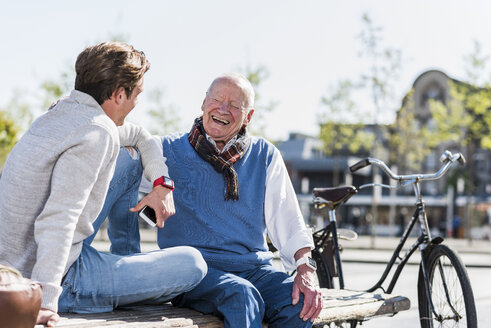 Laughing senior man with adult grandson on a bench - UUF10425