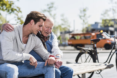 Älterer Mann und erwachsener Enkel auf einer Bank und schauen auf ihre Smartwatches - UUF10426