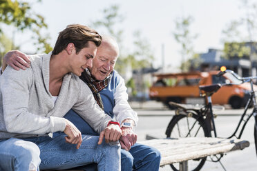 Senior man and adult grandson on a bench looking at their smartwatches - UUF10426