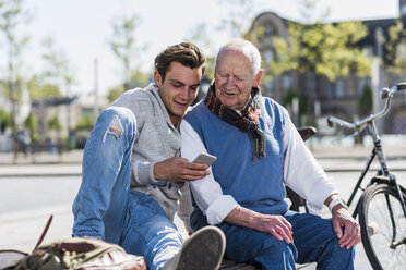 Älterer Mann und erwachsener Enkel auf einer Bank mit Blick auf das Handy - UUF10428