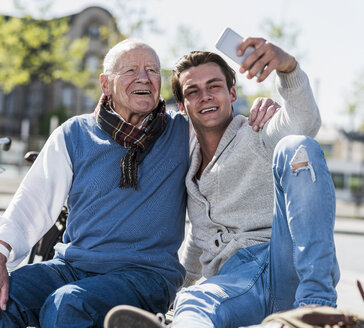 Senior man and adult grandson on a bench taking a selfie - UUF10429