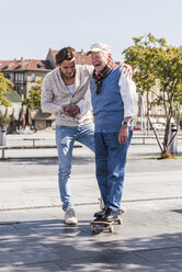 Erwachsener Enkel unterstützt älteren Mann auf Skateboard - UUF10434