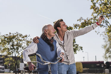 Älterer Mann und erwachsener Enkel machen ein Selfie im Freien - UUF10437